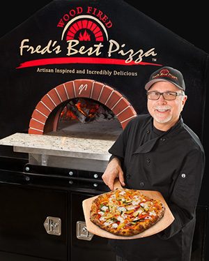 Fred Kominsky showing his passion for wood fired pizza in front of his custom built Mugnaini / Valoriani oven imported from Italy.